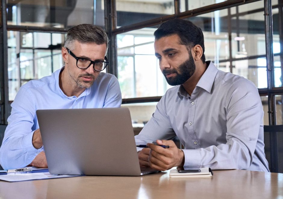 Two diverse business men analysts partners talking, working together, discussing data management using laptop computer. Indian manager consulting client with online technology at office meeting.